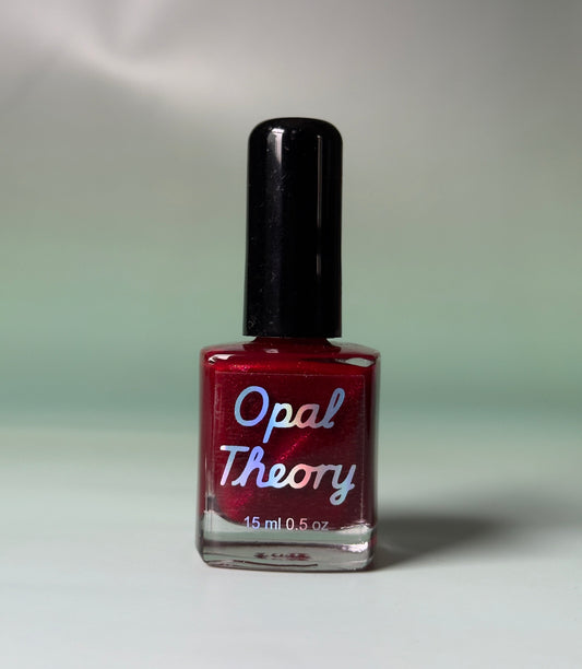Red nail polish bottle with 'Opal Theory' label on a flat surface
