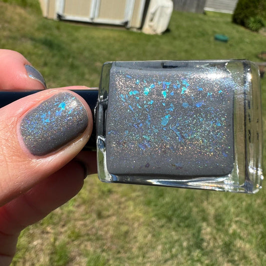 Nail polish with glittery finish held by a hand against a grassy background
Opal theory polish To Artemis with love