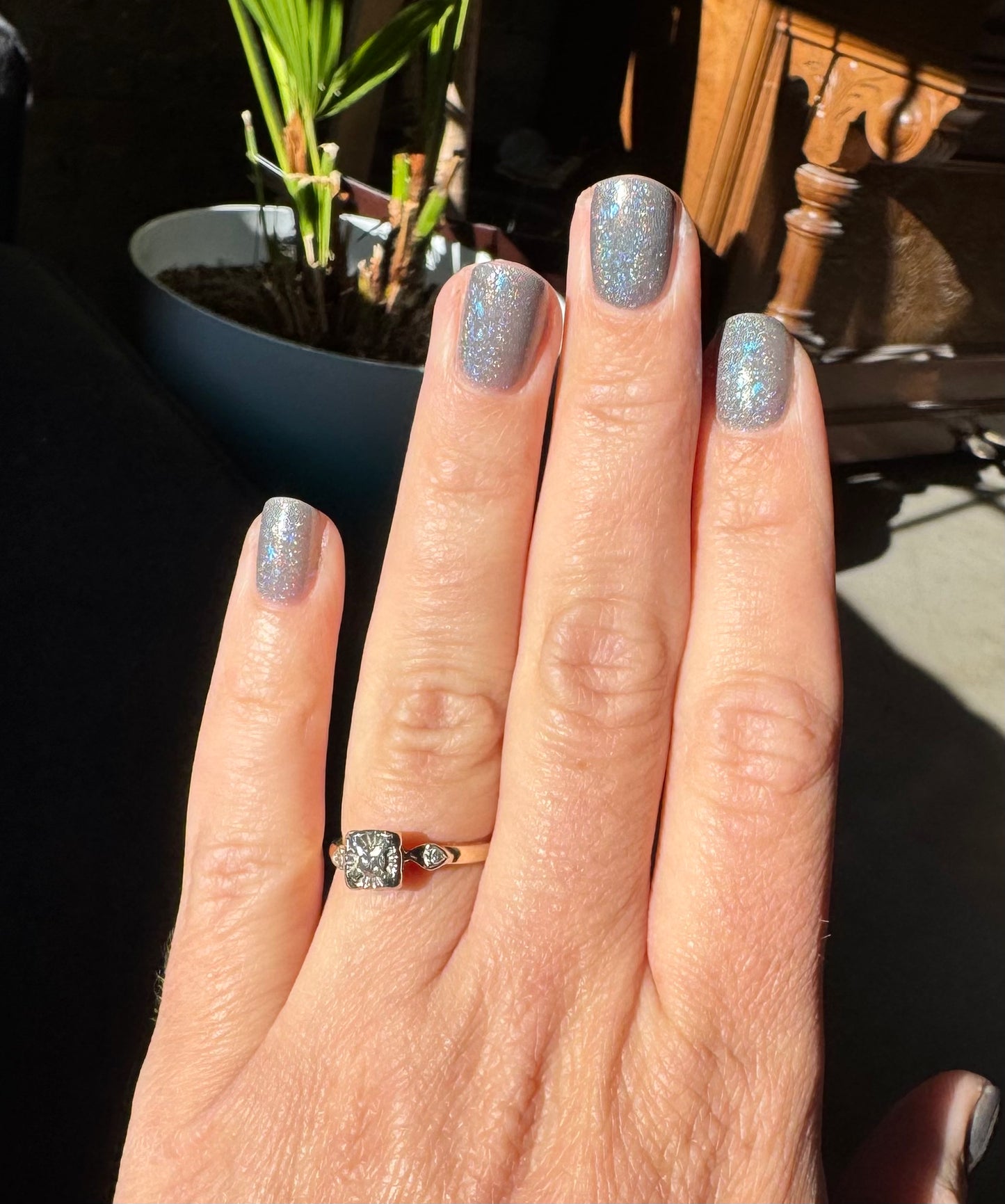 Hand with glittery nail polish and a diamond ring, with a blurred background. Opal theory polish To Artemis with love