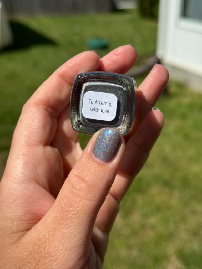 Hand holding a nail polish bottle, bottom facing you. Opal theory polish To Artemis with love