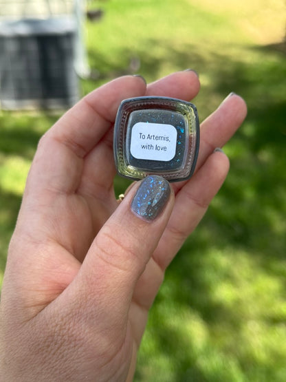Hand holding a nail polish bottle with the bottom facing you. Opal theory polish To Artemis with love