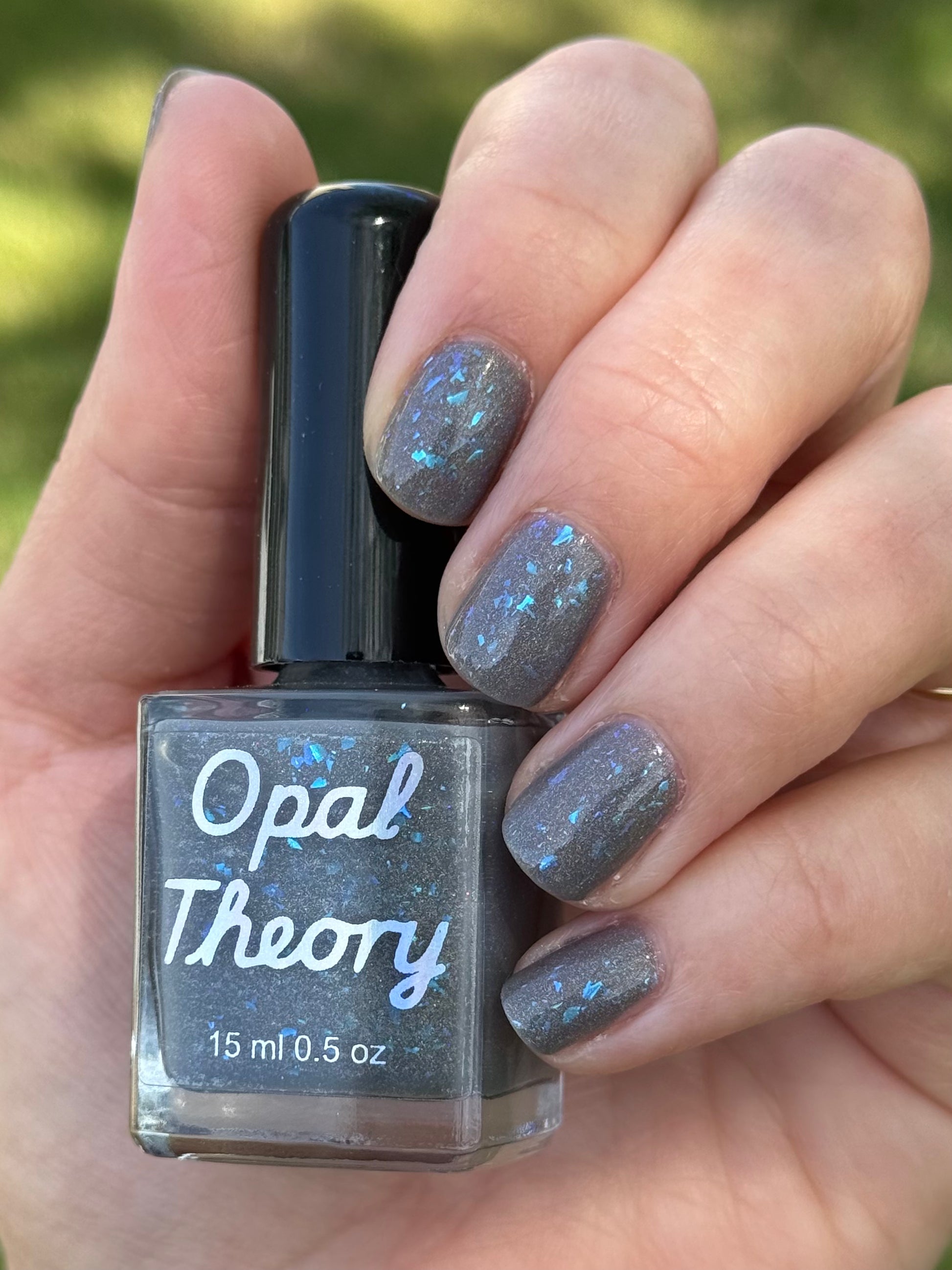 Hand holding a bottle of Opal Theory nail polish with glittery nails.  To Artemis with love
