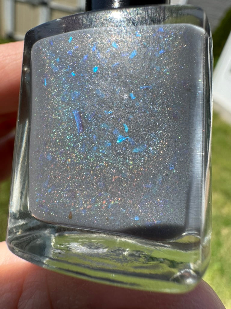 Nail polish bottle with glittery finish held by a hand. Opal theory polish To Artemis with love