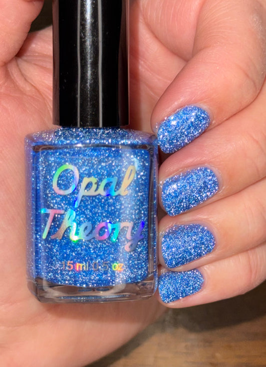 Blue glittery nail polish bottle held by a hand with matching blue glittery nails.
Two if by sea, three if by ICE. ALCU charity nail polish.